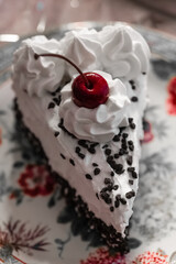 Decadent slice of chocolate cream cake topped with cherry and whipped cream served on floral plate