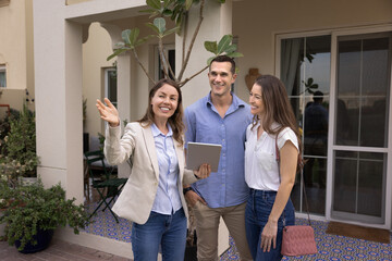 Professional woman realtor presents property to smiling married couple, assisting clients with house selection. Spouses considering purchasing or renting home. Real estate transactions, homeownership