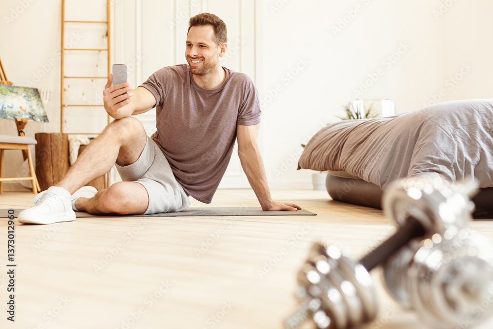Poster workout app. man training using smartphone exercising sitting on gymnastics mat on floor at home. fi