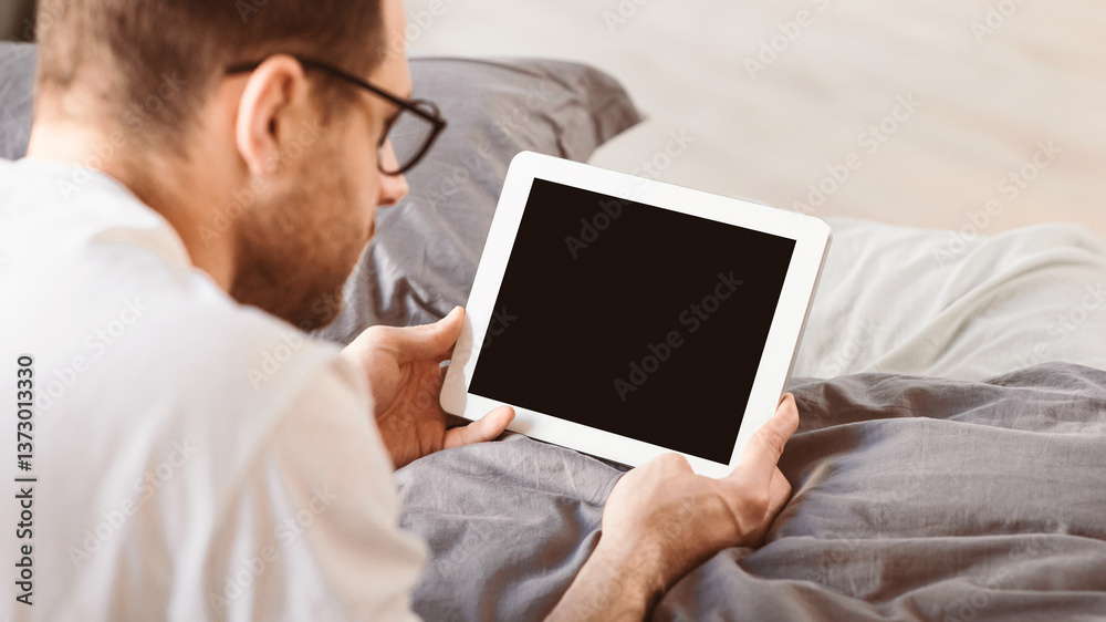 Aufkleber Man Using Digital Tablet With Empty Screen Browsing Internet Lying In Bed In Bedroom At Home. Computer Blank Display For Application And Website Advertisement Concept. Panorama, Mockup