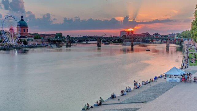 Aerial view of La Grave Hospital with Saint-Pierre Bridge. Port de la Daurade park along the Garonne River timelapse in Toulouse, France. Sunset colorful clouds, ferry at dock and riverside atmosphere