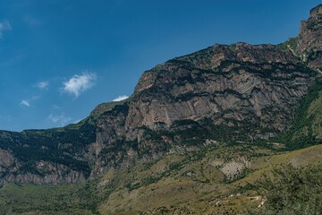 Fototapeta premium Towering cliffs rise dramatically in Northern Ossetia, surrounded by vibrant greenery and a serene blue sky, highlighting the region's natural beauty and geological diversity