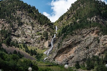 A stunning waterfall flows gracefully from the heights of rugged mountains, surrounded by lush...