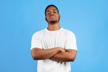 Cool Black Man Standing Crossing Hands Looking At Camera Posing On Blue Studio Background. Menacing...