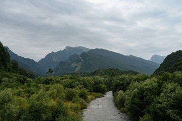 Serene valleys filled with vibrant greenery stretch beneath towering mountains, creating a breathtaking vista in North Ossetia. A winding river flows gently, harmonizing with the tranquil atmosphere