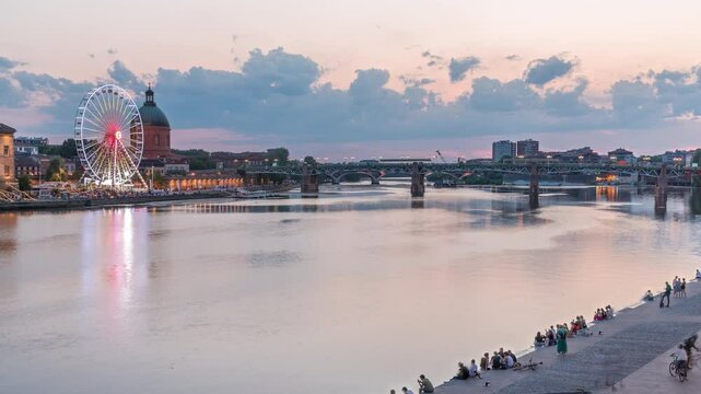 Aerial view of Port de la Daurade park along the Garonne River day to night transition timelapse in Toulouse, France. La Grave Hospital with Saint-Pierre Bridge after sunset with colorful clouds