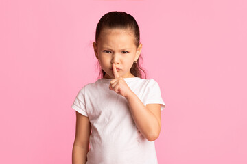 Dont' Speak. Serious asian kid holding finger on lips, free space, isolated over pastel pink studio wall