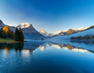 Swiss Alps reflected in the calm blue lake waters at dawn with glowing sunlight and mist over the peaks