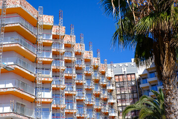 Urban renovation: building under construction with scaffolding and palm trees on a sunny day