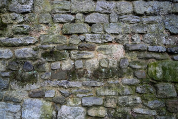 Close-up texture of an ancient, weathered stone wall featuring irregularly shaped blocks, moss growth, and visible mortar, showcasing historic masonry techniques and the patina of age
