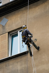 Worker using rope access equipment and safety gear abseils near window on building exterior. Professional maintenance or inspection at height concept