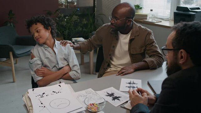 Medium shot of naughty troublemaker boy with bandaged nose and torn shirt refusing to talk to dad and child psychologist after school fight, hyperactivity and adhd