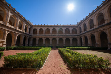 Fototapeta premium Iconic historic courtyard with symmetrical arches and trimmed greenery in Valencia, illuminated by bright sunlight under a clear blue sky.