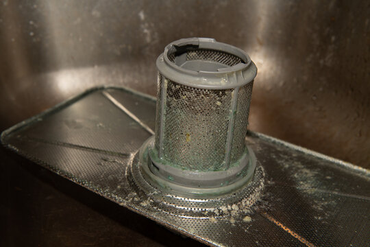 Close up view of a dirty dishwasher filter requiring urgent cleaning, revealing mold, food debris, and buildup of grime and bacteria