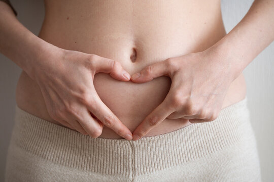 Woman forming a heart shape with her hands on her belly, celebrating body positivity and embracing fertility and motherhood