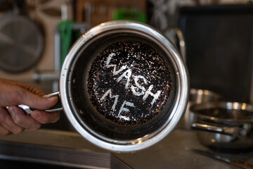 Person holding a dirty burnt pot with the words Wash me written on the bottom