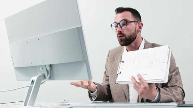 A business man is working and videoconferencing at a computer. Shows growth chart on paper. Concept of remote working, video conferencing and successful business.