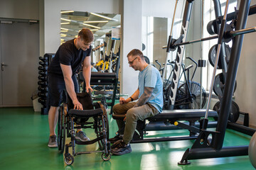 Dedicated trainer helps disabled athlete move safely into wheelchair following rigorous workout. Inclusive male comfort and wellbeing, sports coach provides support guidance during exercises in gym