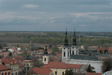 Panoramic view of Sremski Karlovci, Serbia, featuring Saint Nicholas Cathedral, historic baroque buildings, and the Danube River. Captured in spring under dramatic cloudy skies.