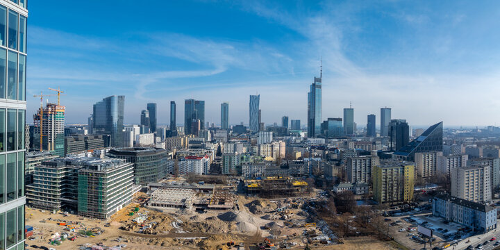 Aerial view of Warsaw, Poland, featuring Varso Tower, skyscrapers, mid rise buildings, and an active construction site under a clear blue sky.