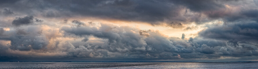 Panoramaaufnahme des dramatischen Himmels bei Sturm mit Wolkenfetzen über dem Watt bei beginnender...