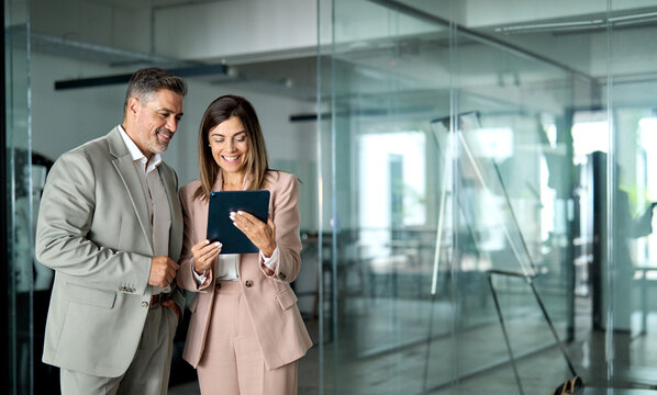 Professional business executives team working using digital tablet computer standing in office. Two middle aged colleagues managers discussing smart technology at corporate meeting. Copy space.