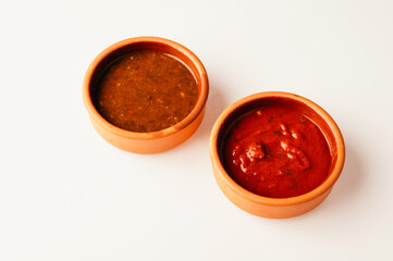 A pair of flavorful sauces, one spicy and one mild, displayed in terracotta bowls on a clean surface.