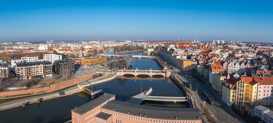 Obraz premium Aerial view of Wroclaw, Poland, showcasing the Oder River, multiple bridges, red roofed historic buildings, Gothic church towers, and urban architecture.
