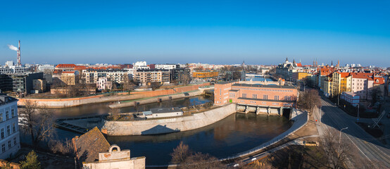 Aerial view of Wroclaw, Poland, showing the Oder River, a red brick water management structure, colorful facades, red tiled roofs, and church spires.