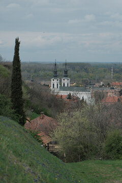 Scenic view of Saint Nicholas Cathedral in Sremski Karlovci, Serbia, seen from a grassy hillside with blooming spring flowers. Blend of nature, history, and Balkan town architecture.