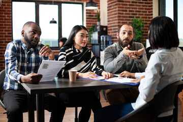 Multiethnic HR executives interview black woman for a position, focusing on her resume. Recruitment agency team reviews a female candidate CV, asking questions and discussing potential contract.