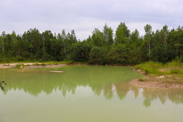 Chalk quarry in Latvia. Forest near turquoise lake. Green water.