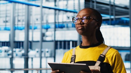 Industry 4.0 plant technician monitors system performance using digital device app. Smart factory engineer oversees operation of robotic arms and conveyor belts using software on tablet, camera A