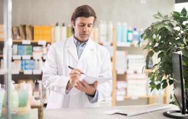 Man pharmacist makes restock, uses paper carrier of information. Checking availability of drugs,...