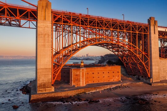 Golden Gate Bridge, USA, at sunset. The iconic bridge spans the strait, connecting San Francisco. Fort Point sits beneath, with people enjoying the beach.