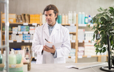 Man pharmacist makes restock, uses paper carrier of information. Checking availability of drugs,...