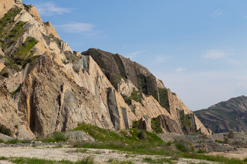 Mountain Majesty: Jagged, layered cliffs and patchy greenery form nature's ancient canvas under a clear, sunlit sky.