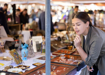 Portrait of glad smiling young woman choosing vintage goods at flea market