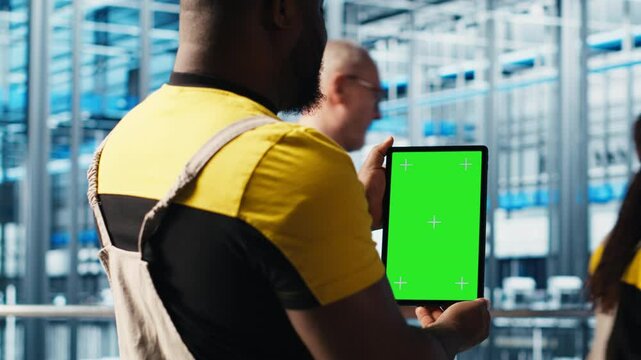 Smart factory expert using green screen tablet to test automated systems and ensure reliability. Worker uses chroma key device to identify bottlenecks and optimize gear based on sensors data, camera A