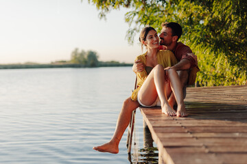 Happy couple relaxing and enjoying a romantic sunset on a lake pier