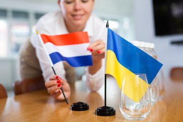 Female hands arranging national flags of Netherlands and Ukraine on table before international...