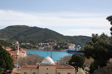 A vibrant harbor showcases a large cargo ship alongside smaller boats, nestled between green hills...
