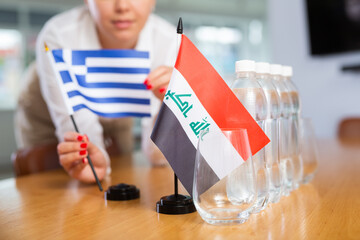Employee of delegation prepares negotiating table - sets up the flag of Greece and Iraq