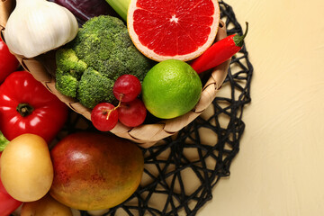 Wicker basket with different fresh fruits and vegetables on yellow background, closeup