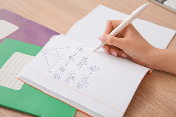 Woman writing math formulas in copybook on wooden table