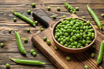 Bowl and board with fresh green peas on wooden background