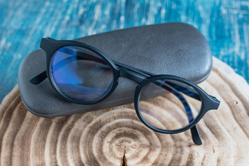 Transparent optical glasses with glasses case on wooden stump.Top view.