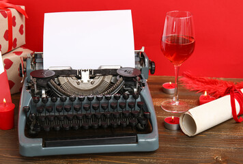 Beautiful composition with vintage typewriter, glass of wine and candles for Valentine's day on table near red wall
