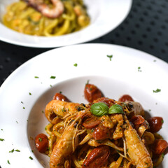 spaghettoni di pasta fresca con gamberi e pomodori rossi, serviti in un piatto bianco al ristorante