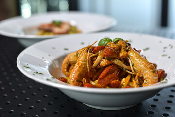 spaghettoni di pasta fresca con gamberi e pomodori rossi, serviti in un piatto bianco al ristorante